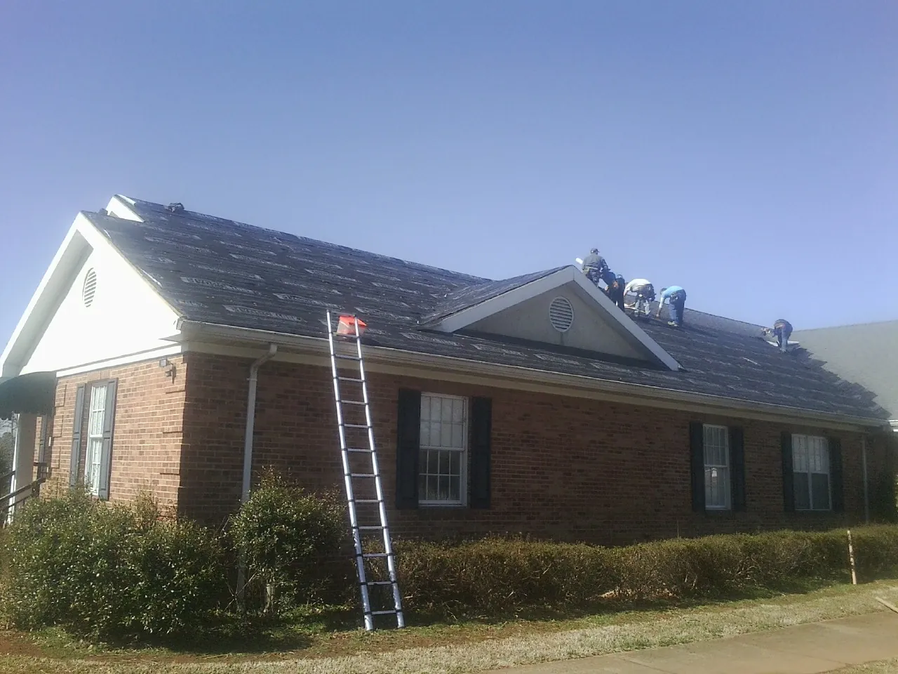 Crew tearing shingles off a brick ranch roof with a ladder set — Emergency Roof Repair work by our crew in Millbrae