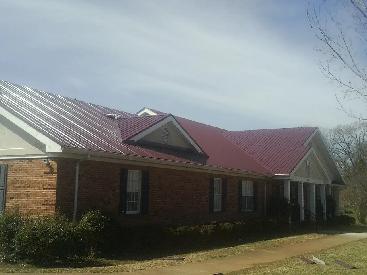 Red metal roof with gabled entries on a long brick building, from a Hail Damage Roof Repair job in Millbrae