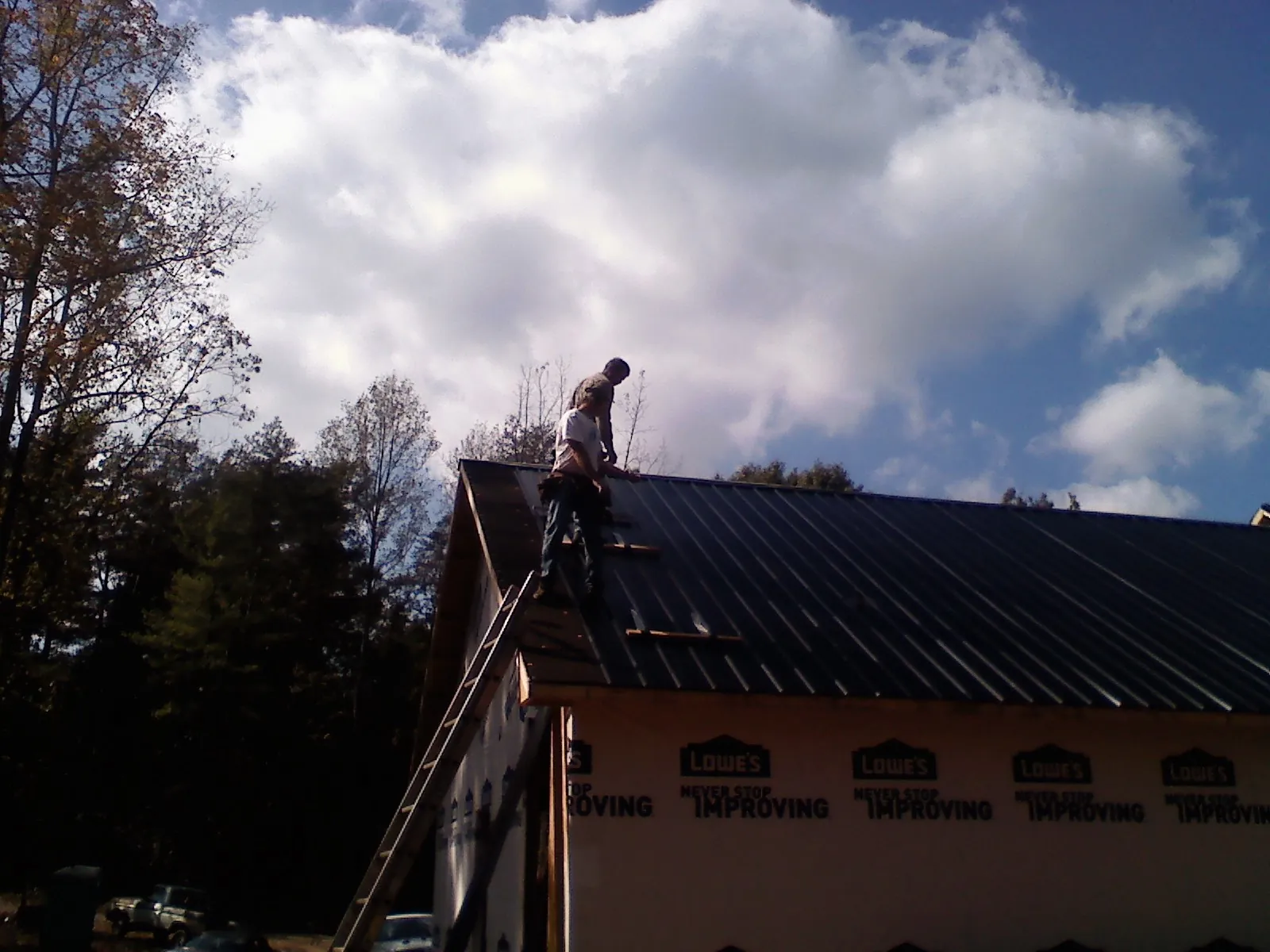 Roofer fastening dark metal panels high against a cloudy sky, from a Roof Inspection job in Millbrae