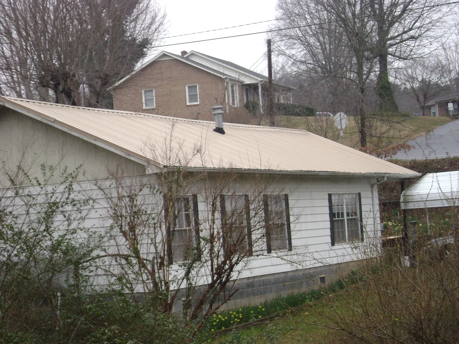 Tan metal roof on a white sided house set into a hillside — Commercial Roofing by Roofing Brothers in Millbrae